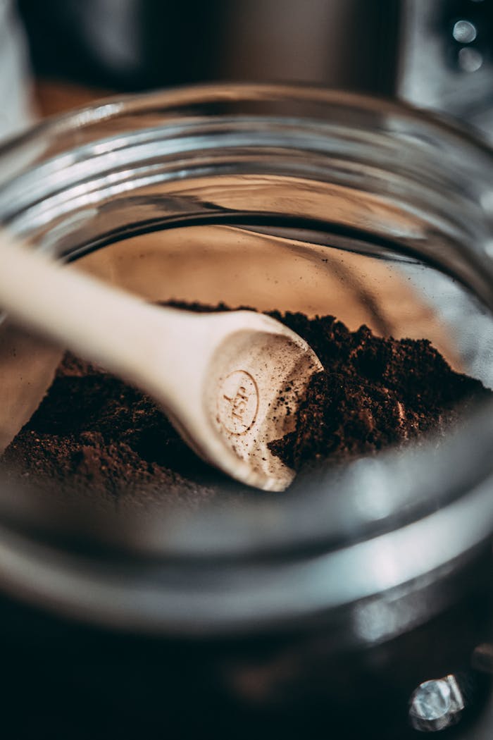 services-img Wooden spoon resting in dark coffee grounds inside a glass jar.