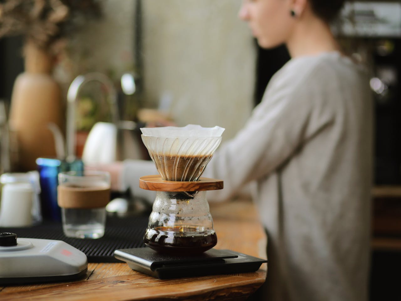 Close-up of pour-over coffee brewing with a clear glass dripper indoors, capturing a warm, cozy feel.