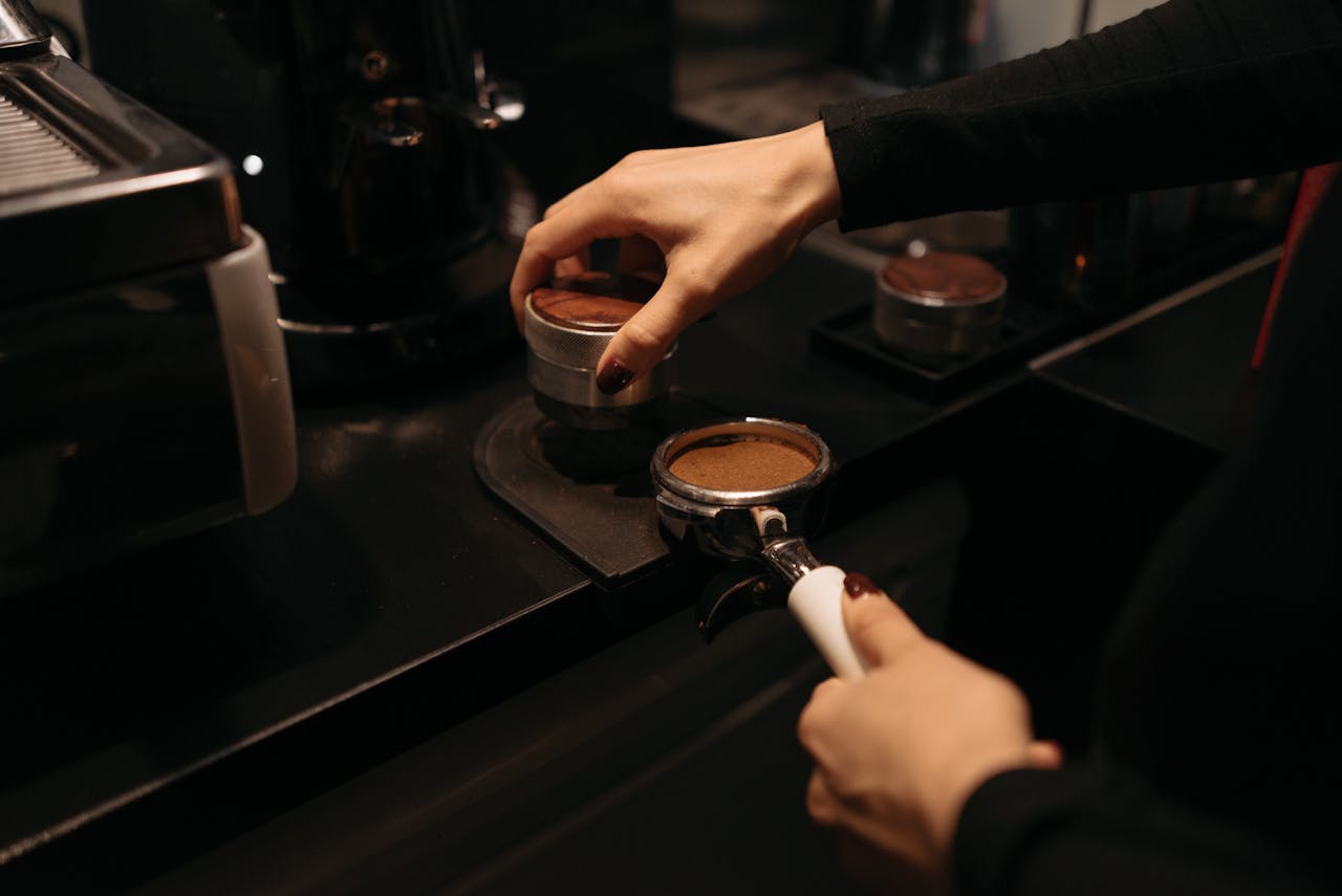 Barista tamping espresso with a portafilter in a coffee shop setting.