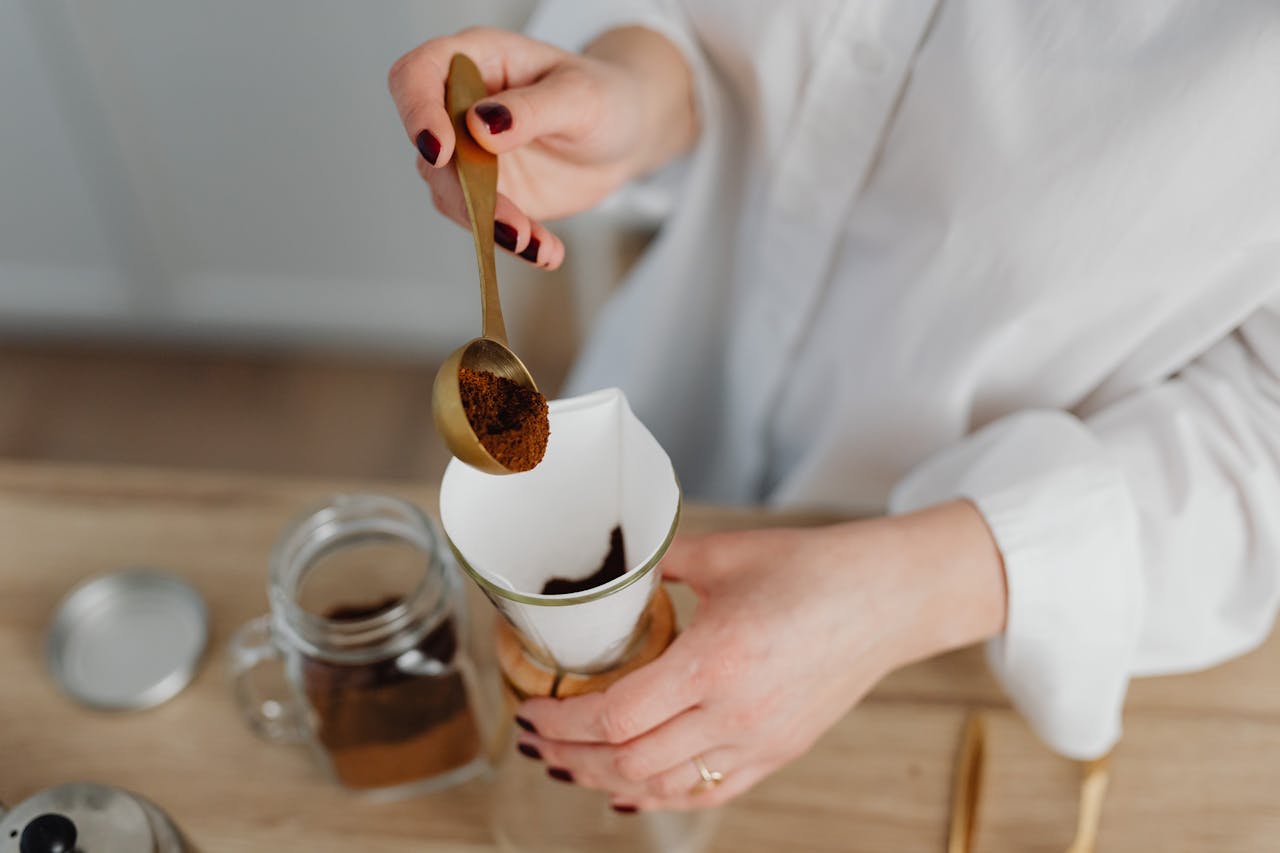 Woman adding coffee grounds to a filter with a spoon over a wooden surface.